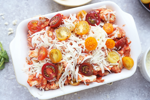 The cauliflower caprese casserole in a white baking dish topped with mozzarella and sliced cherry tomatoes