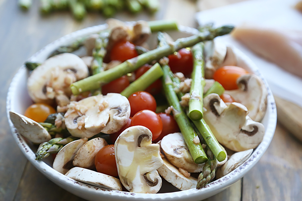 Sliced mushrooms, asparagus, and cherry tomatoes tossed in garlic vinaigrette in a large bowl