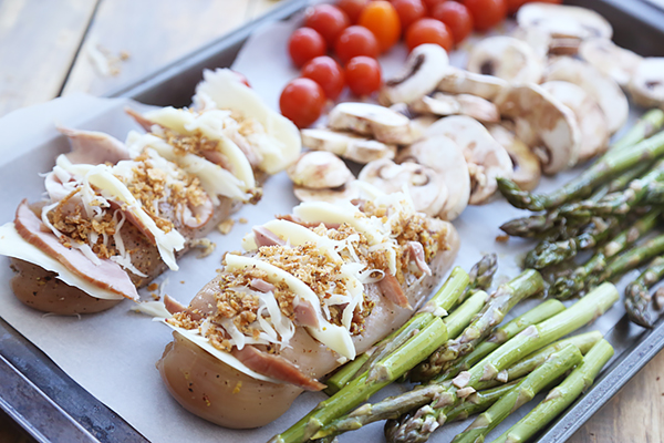 Hasselback chicken stuffed with ham and mozzarella on a sheet pan with asparagus and mushrooms