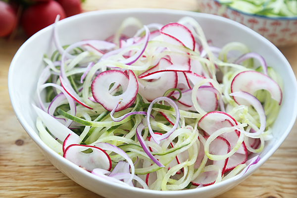 Spiralized cucumber noodles, thinly sliced radishes, and red onion rings tossed in a mixing bowl