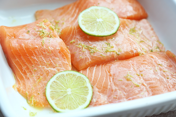 Raw salmon fillets with lime slices and zest in a white baking dish with marinade