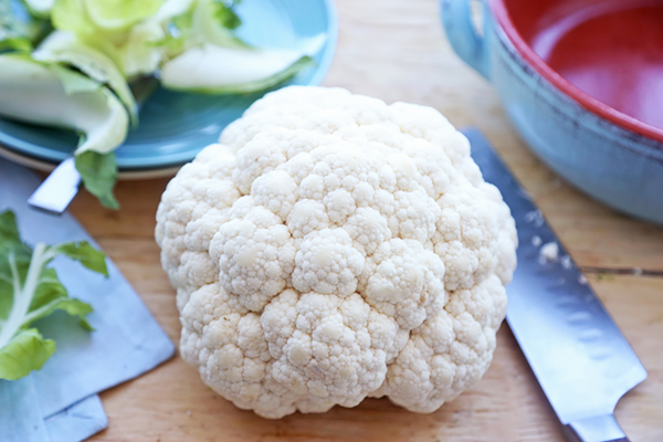 Whole cauliflower head with leaves trimmed, sitting on a cutting board