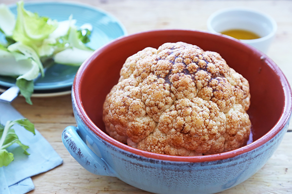 Whole cauliflower brushed with olive oil, cumin, and chili powder in a ceramic dish