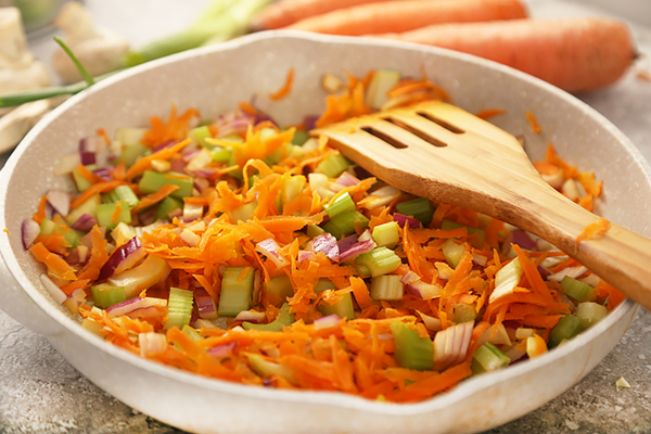 Shredded carrots, sliced red onion, and chopped celery sauteing in a saute pan