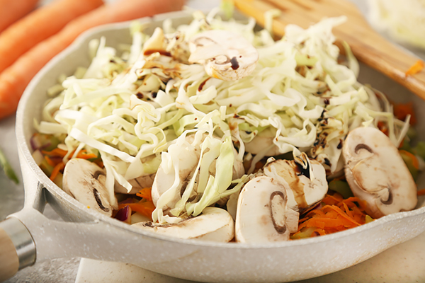 Green cabbage and mushrooms layered over carrots and celery before covering to cook