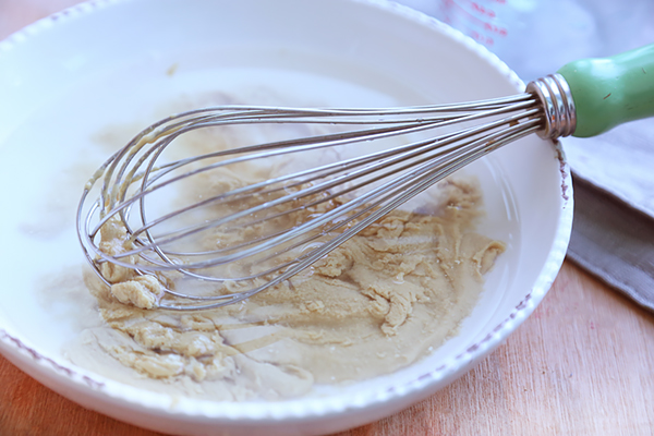Whisking tahini and water together into a thick paste in a white bowl