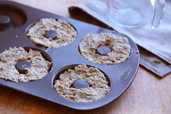 Raw bagel dough pressed into four wells of a donut pan