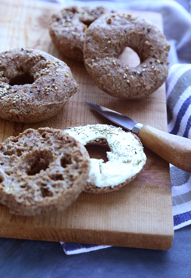 Baked keto bagels with sesame seeds on a cutting board, one halved and spread with cream cheese
