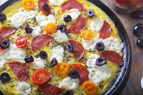 Egg crust pizza layered with pepperoni, mozzarella, black olives, and cherry tomatoes in a cast iron skillet