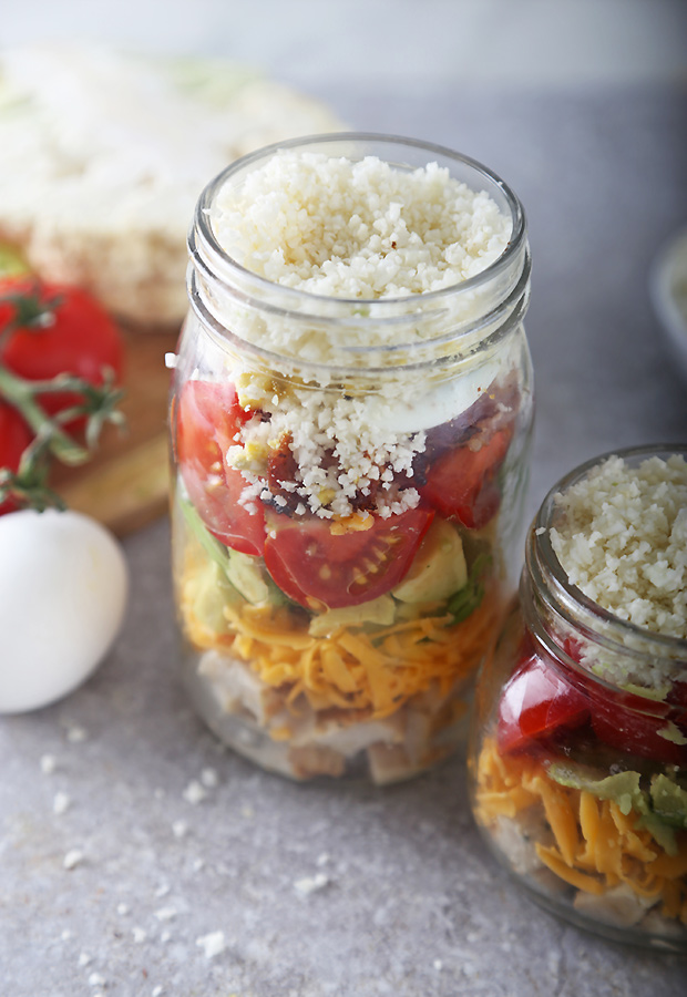 Sealed chicken cobb salad jars showing layers of cheddar, tomato, avocado, and a cauliflower base
