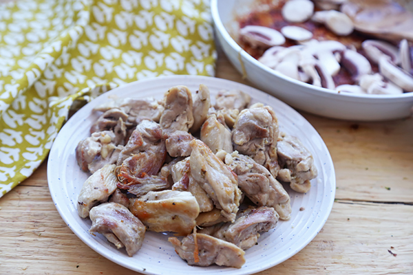 Browned chicken thigh strips piled on a white plate after pan-frying