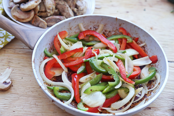 Sliced red and green bell peppers with onion sauteing in a skillet