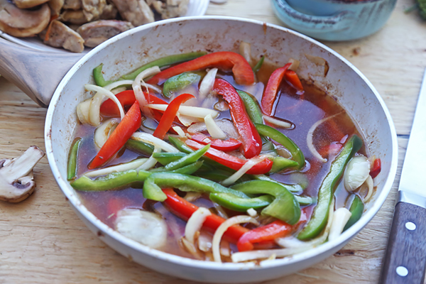 Chicken broth poured over bell peppers and onion in a saute pan