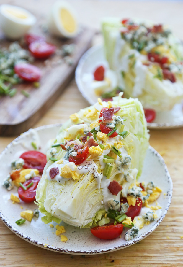 Iceberg lettuce wedges topped with bacon, cherry tomatoes, chopped egg, blue cheese, and chives
