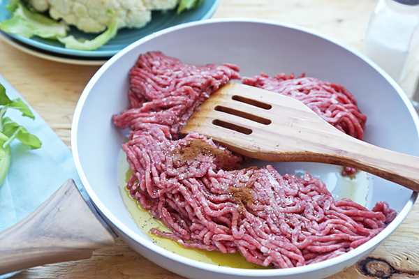 Ground beef and cinnamon browning in olive oil in a skillet with a wooden spatula