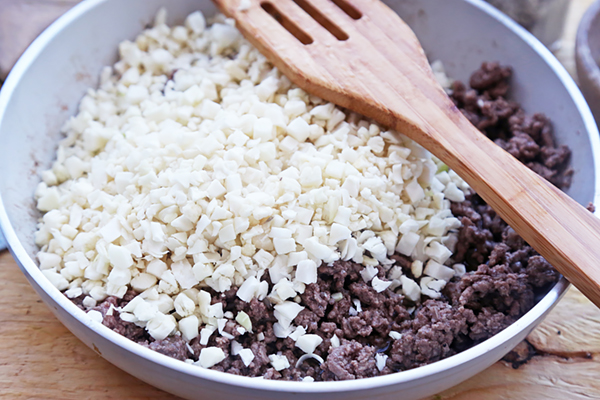 Cauliflower rice stirred into browned ground beef in a skillet