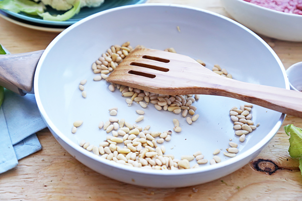 Pine nuts toasting in a dry skillet with a wooden spatula