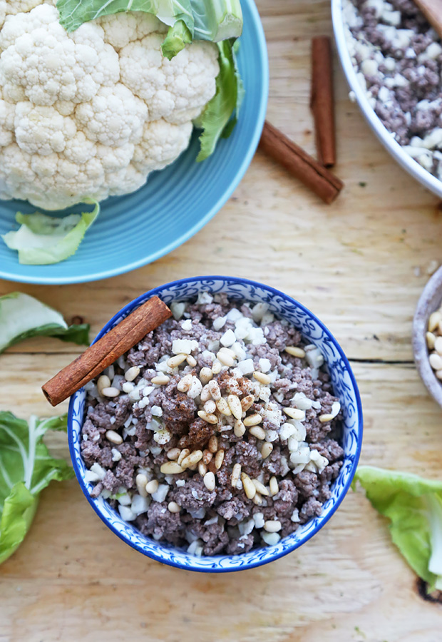 Cauliflower rice pilaf with ground beef, toasted pine nuts, and a cinnamon stick in a blue bowl