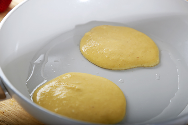 Two small almond flour pancakes cooking in a lightly oiled white pan