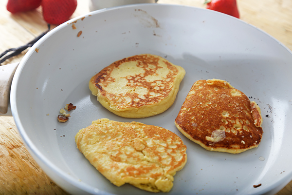 Three almond flour pancakes browning after flipping in a skillet