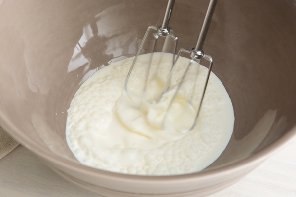 Whipping heavy cream with electric beaters until soft peaks form in a gray bowl