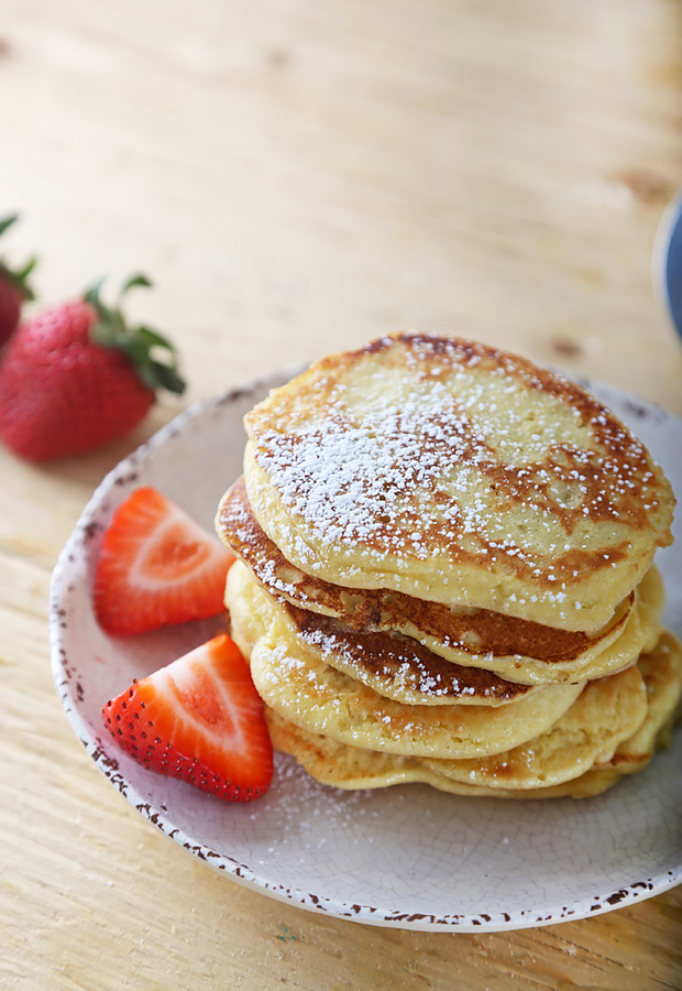 Stacked golden keto pancakes dusted with powdered sweetener beside fresh strawberry halves