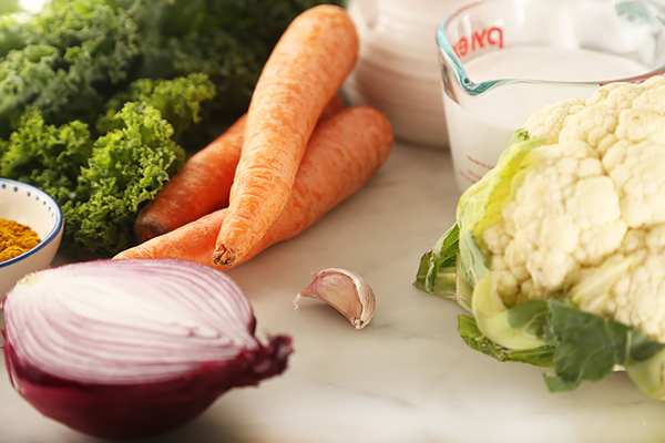 Cauliflower, kale, carrots, red onion, garlic, and curry powder gathered on a marble counter