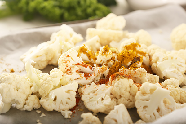 Raw cauliflower florets on a parchment-lined baking sheet with curry powder and paprika sprinkled on top