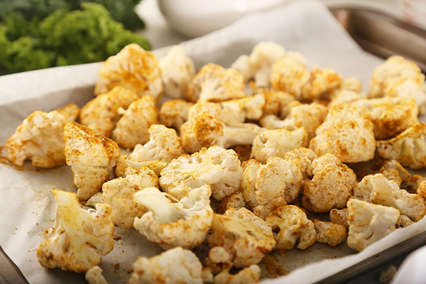 Roasted cauliflower florets coated in curry powder and paprika on a baking sheet