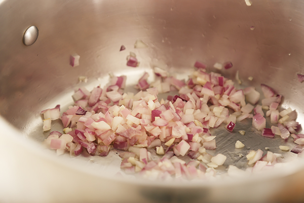Diced red onion and minced garlic sauteing in a stainless steel stock pot