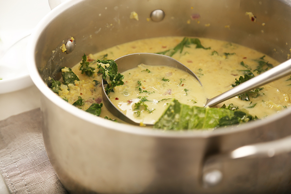 Ladle stirring curry cauliflower soup with kale and red pepper flakes in a stock pot