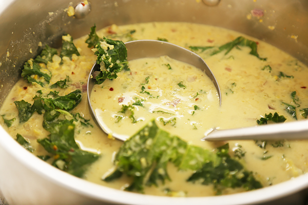 Simmering cauliflower and kale curry soup with visible red pepper flakes in a steel pot