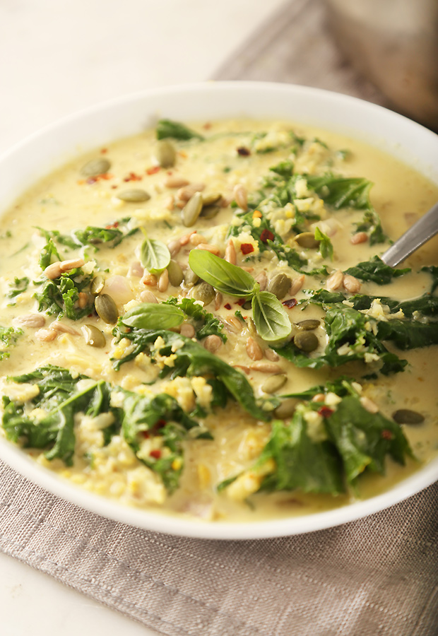 Bowl of cauliflower kale curry soup topped with pumpkin seeds, sunflower seeds, and fresh basil