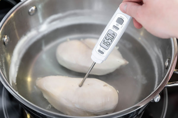 Checking poached chicken breast temperature at 165F with a digital thermometer