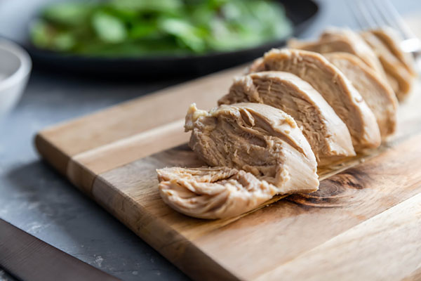 Sliced poached chicken breast fanned out on a wooden cutting board