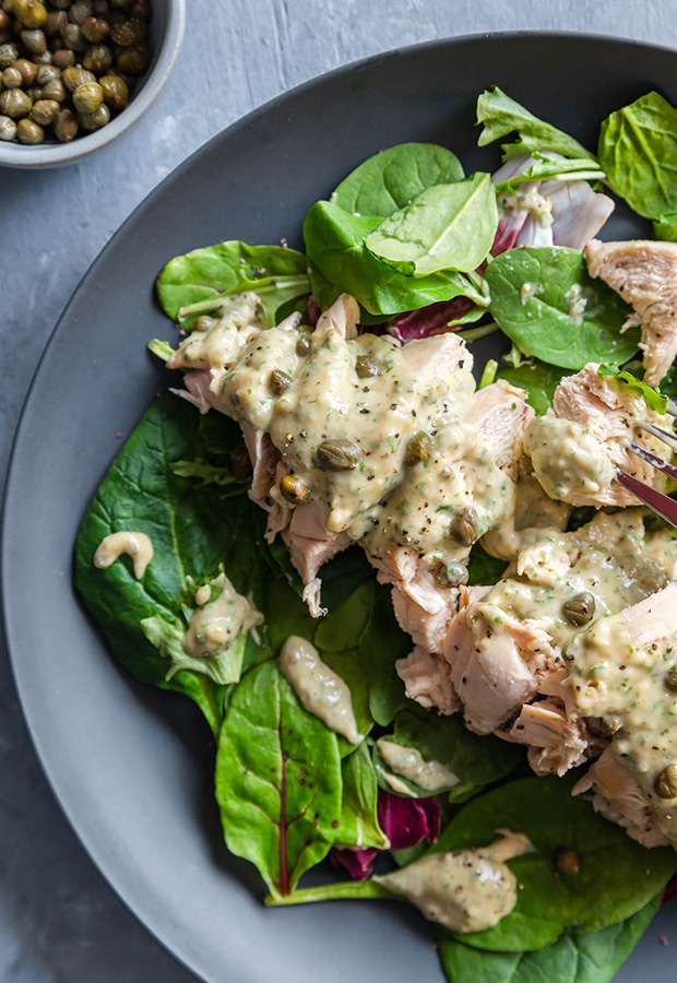 Thin-cut chicken and spring mix on a gray plate topped with tonnato sauce and capers