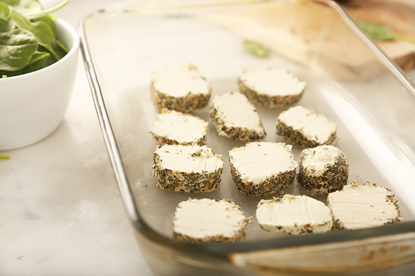 Herb-crusted goat cheese rounds arranged in a glass baking dish