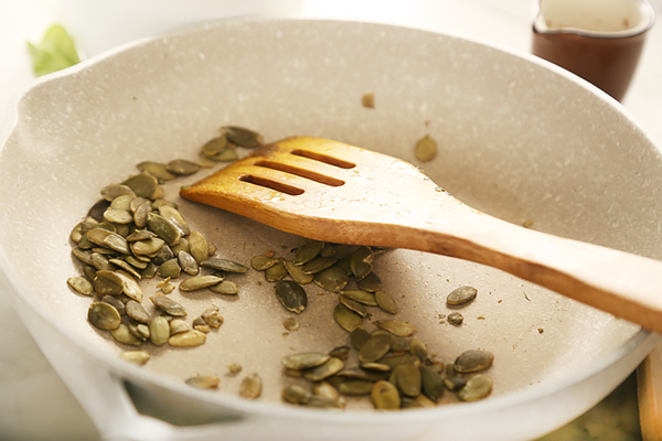 Pumpkin seeds toasting in a dry skillet with a wooden spatula