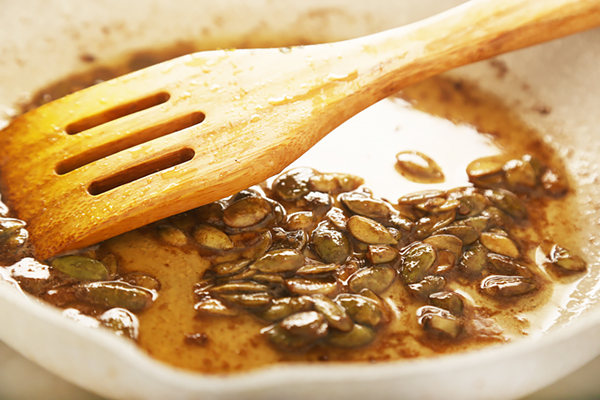 Pumpkin seeds simmering in browned butter and balsamic vinegar in a wide pan