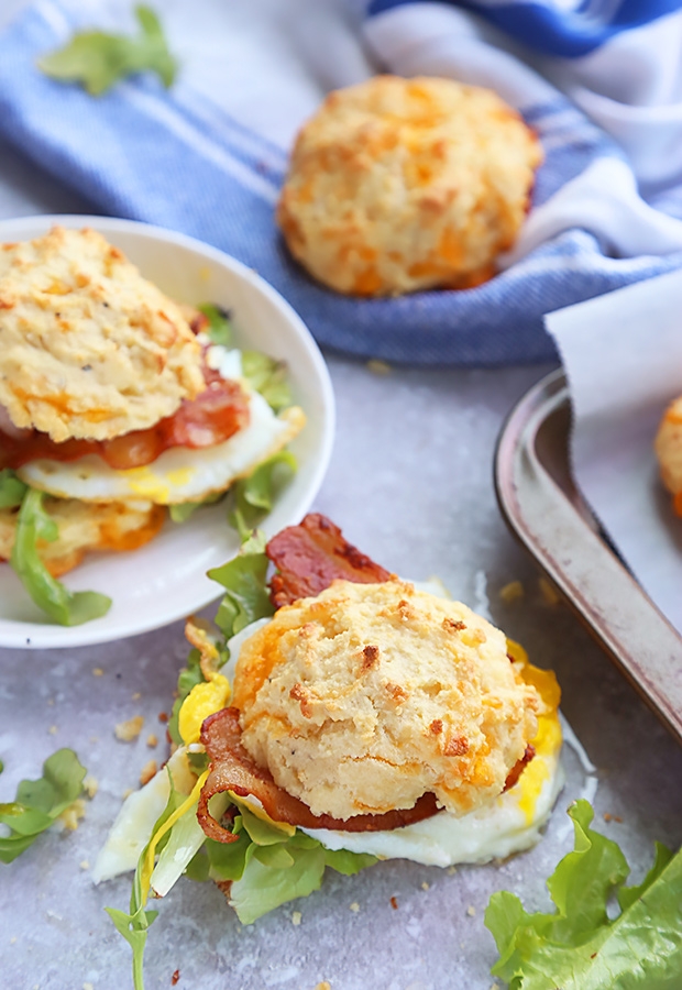 Cheddar almond flour biscuit sandwiches layered with fried egg, bacon, and mixed greens