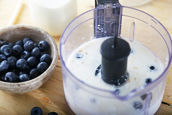 Blueberries and coconut milk blending in a food processor with whole berries beside