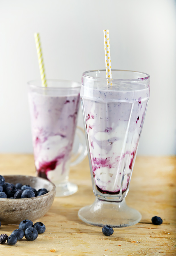 Two tall glasses of blueberry smoothie with purple swirls and polka-dot straws