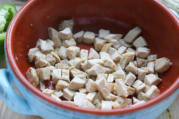 Browned cubed chicken seasoned with Cajun spices in a red ceramic pot