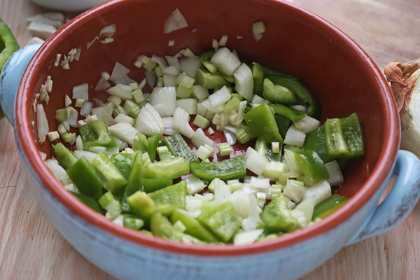 Diced onion, celery, and green bell pepper sauteing in a red ceramic pot