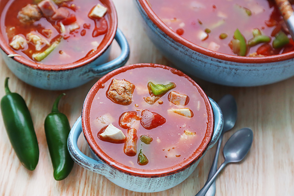 Tomato-based jambalaya soup with chunks of sausage, ham, and green pepper in red ceramic bowls