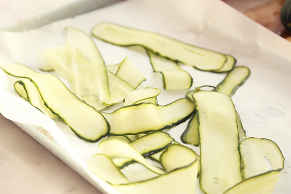Thin cucumber slices cut lengthwise on a mandolin laid out on parchment paper
