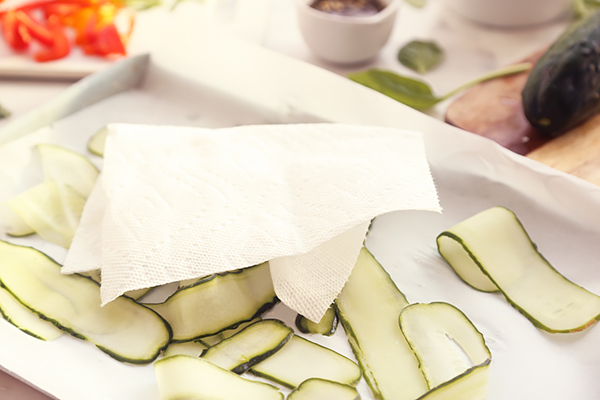 Patting mandolin-sliced cucumber ribbons dry with a paper towel on parchment