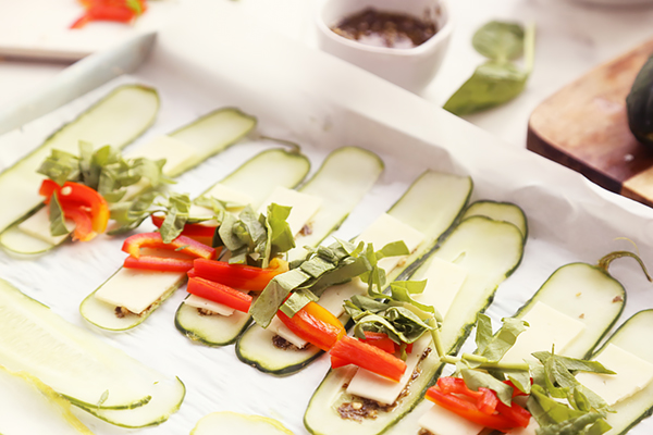 Cucumber slices layered with pesto, mozzarella, red bell pepper, and spinach before rolling