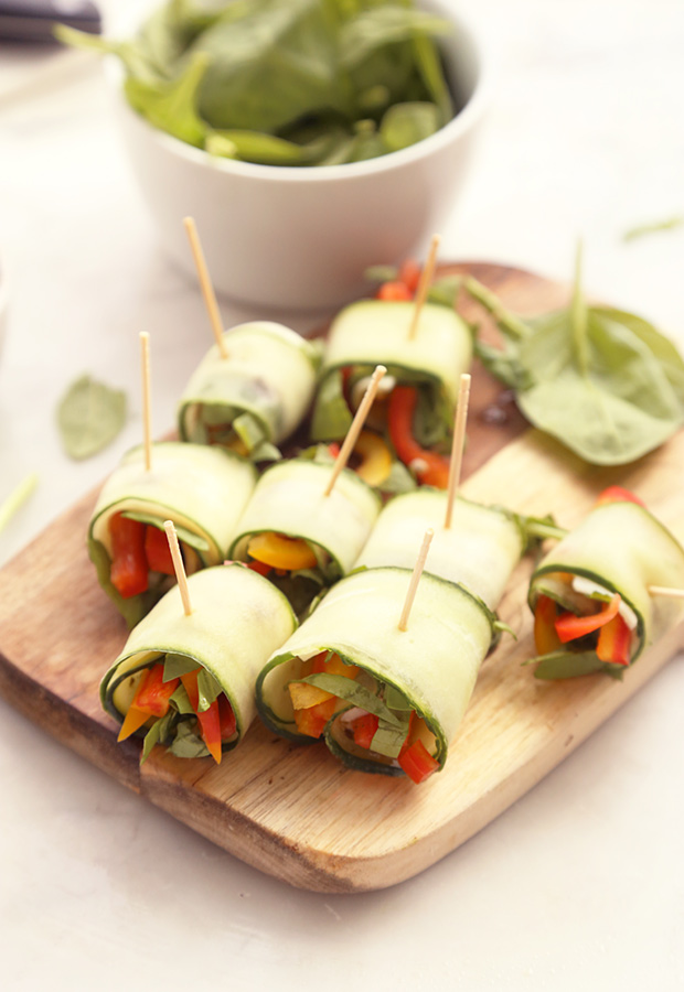 Cucumber roll-ups secured with toothpicks on a wooden cutting board, spinach and peppers peeking out