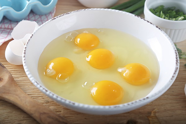 Five raw eggs cracked into a white mixing bowl with yolks intact